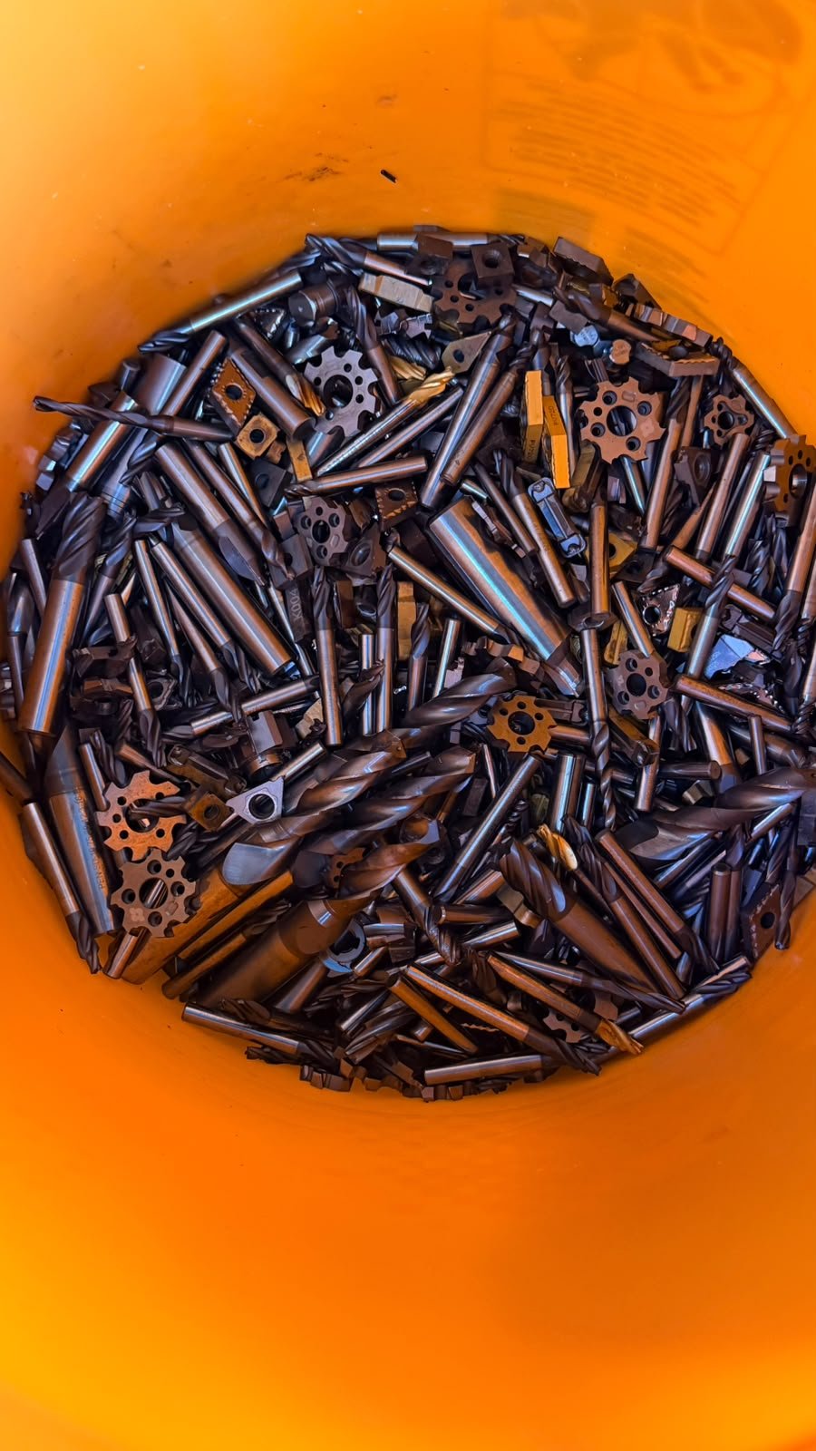Bulk tungsten carbide tools and inserts in an orange bucket.