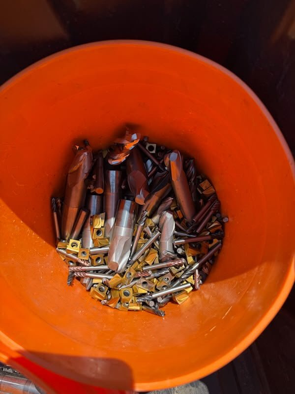 Mixed carbide inserts and end mills in an orange bucket.