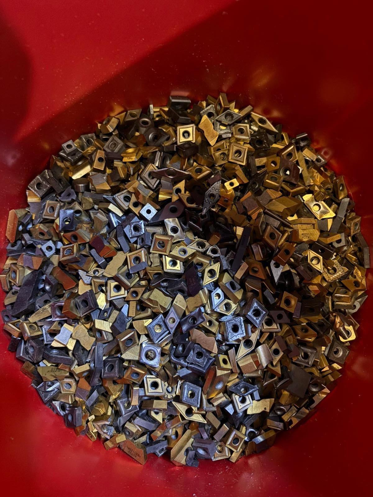 Sorted carbide inserts in a red bin for Canadian scrap quote review.